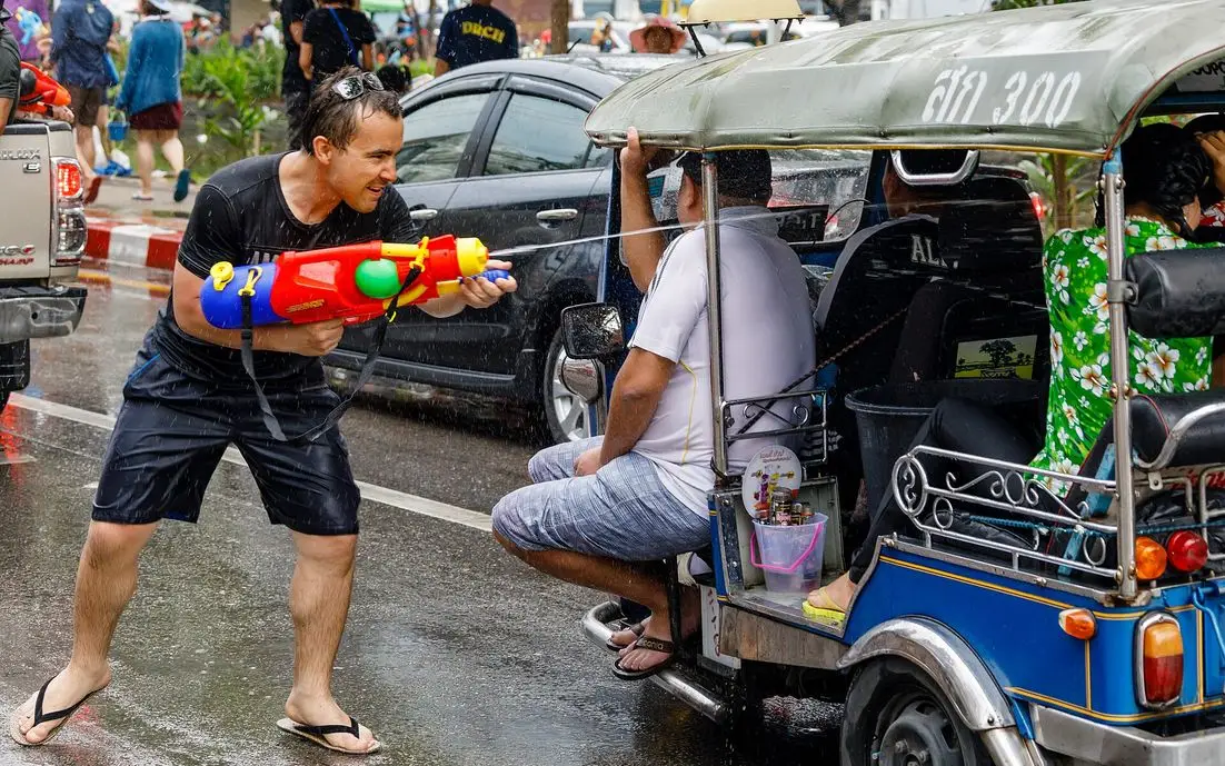 A man fires a large water gun at tuk-tuk passengers on the wet moat road in Chiang Mai during Songkran