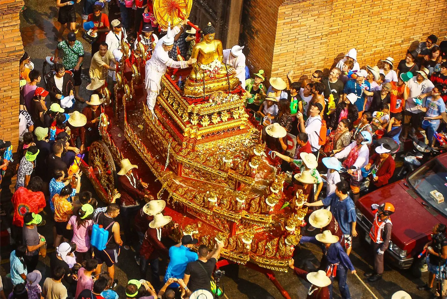The gilded Phra Buddha Sihing procession cart passing through the old brick city gate in Chiang Mai, surrounded by a crowd