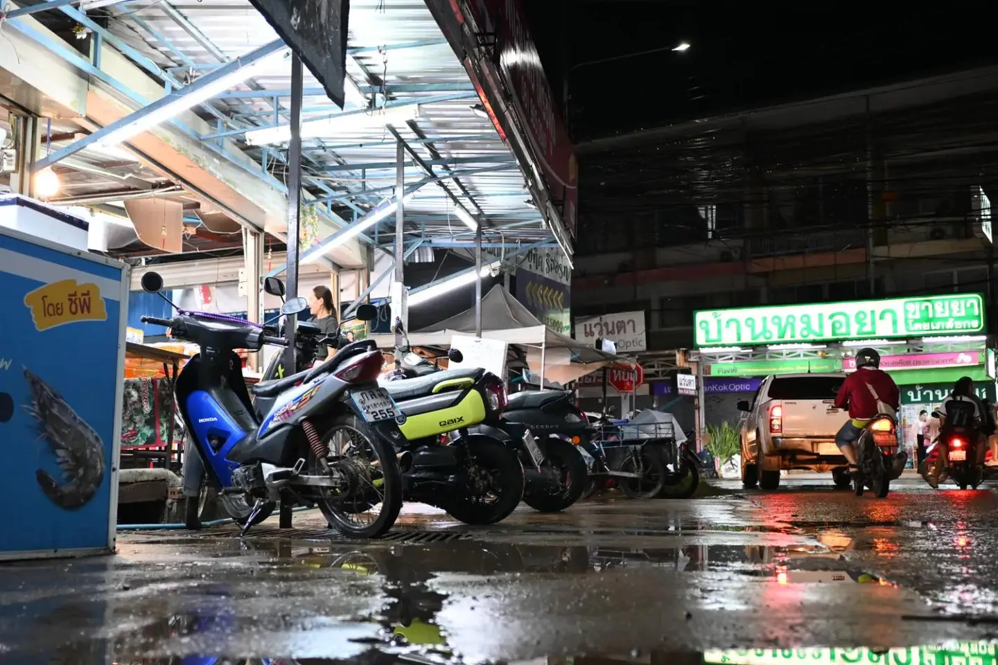 A rain-slicked Thai street at night with parked scooters