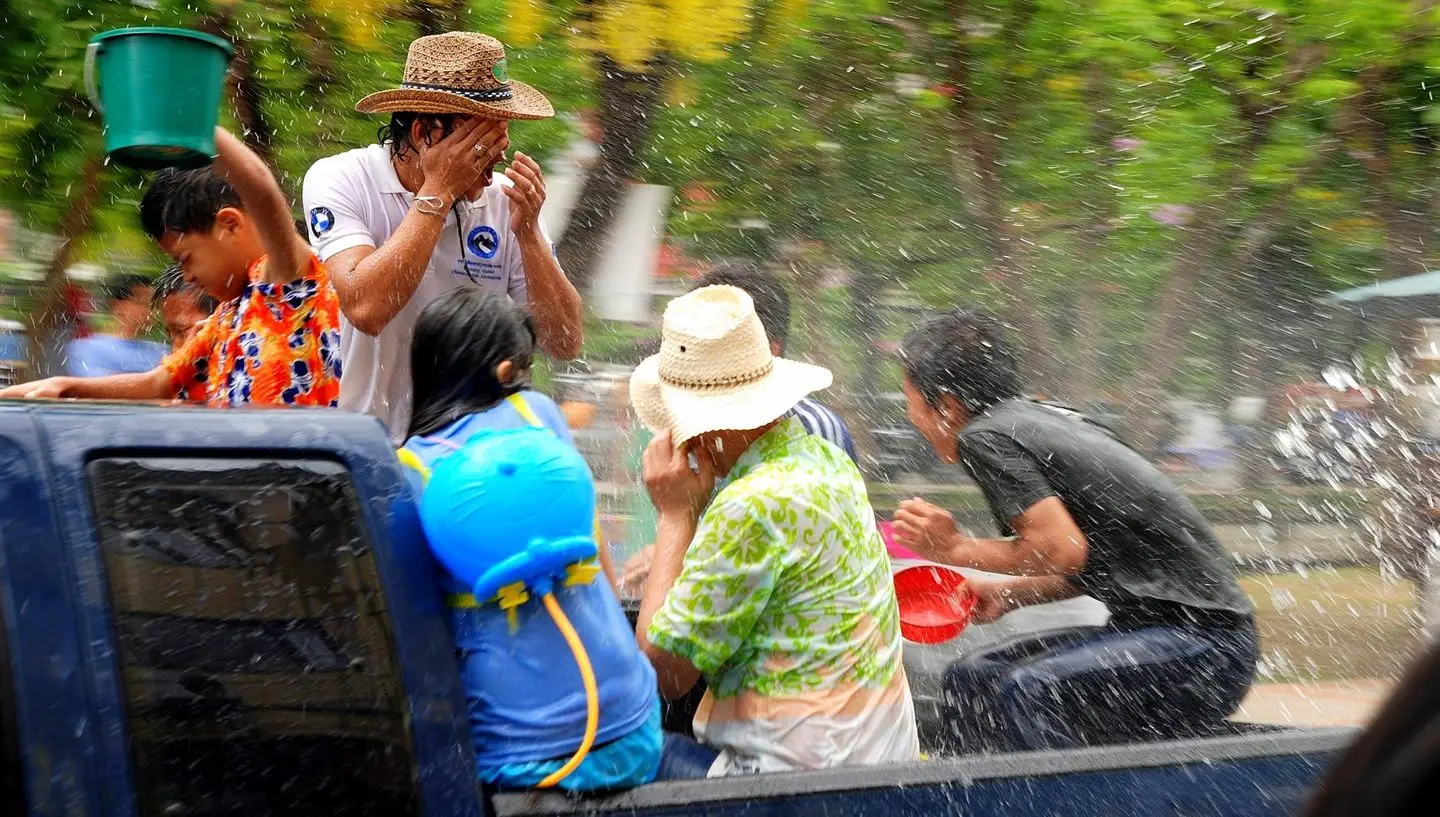 People in the back of a pickup truck getting soaked with buckets of water at Songkran in Chiang Mai