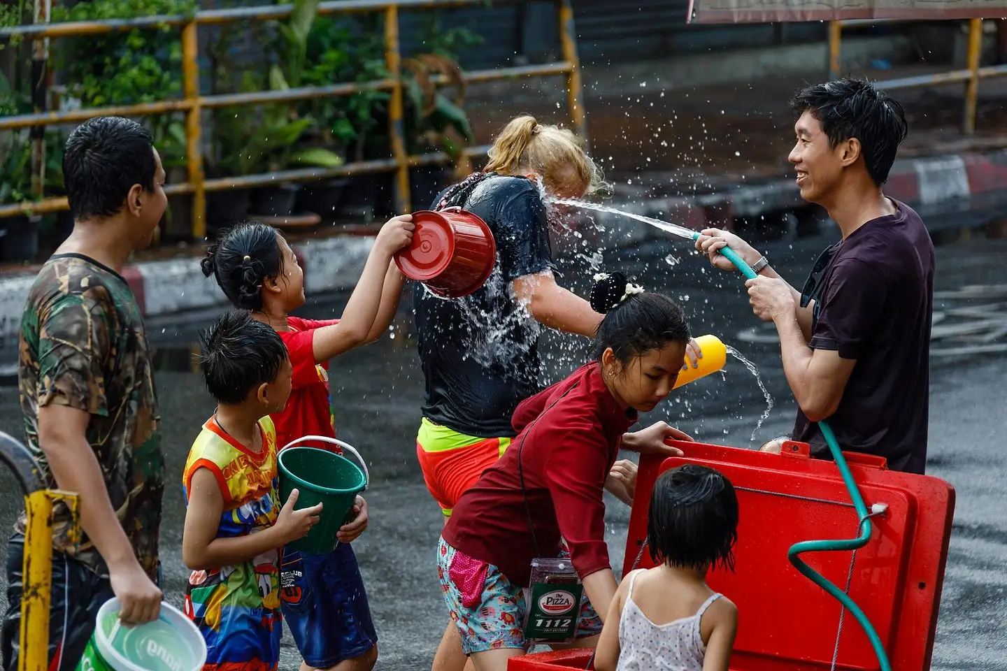 A Thai family with a hose, buckets and a red water tank drenching a visitor on a Chiang Mai street at Songkran