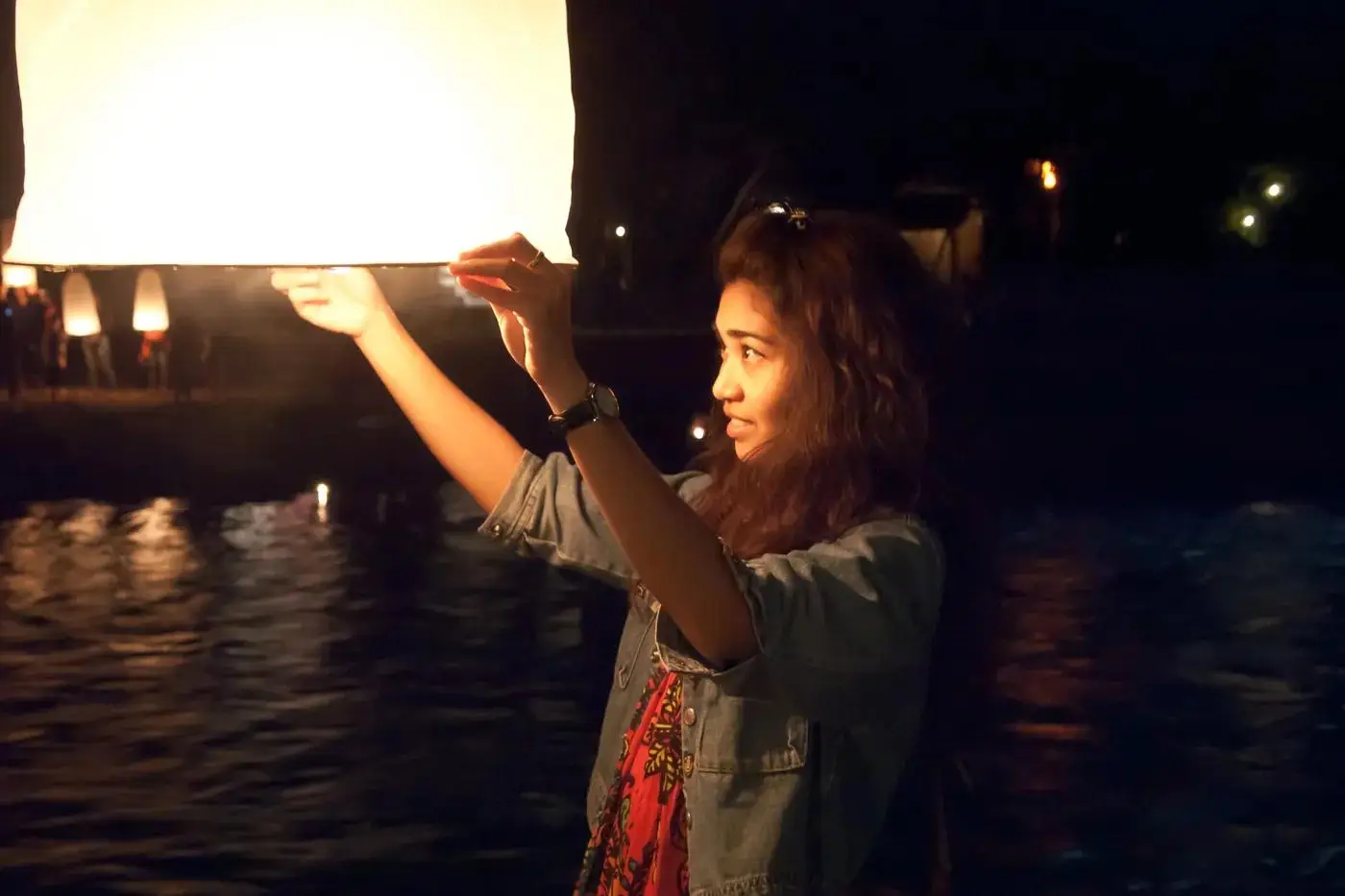 A woman about to release a lantern by the Ping River at night